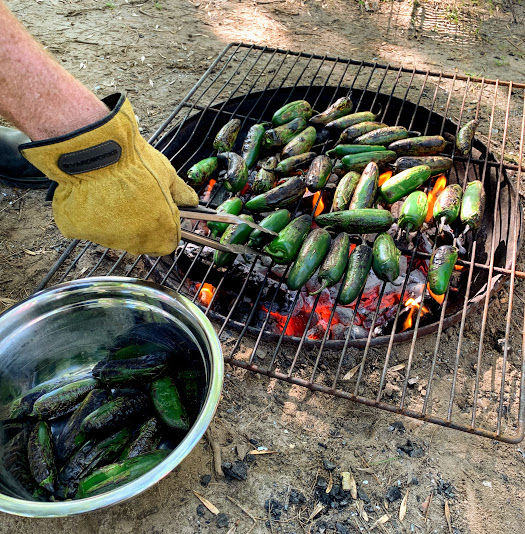 Colin uses tongs to roast jalapenos over the fire