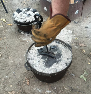 A cast iron dutch oven with a lid covered in ash from charcoal